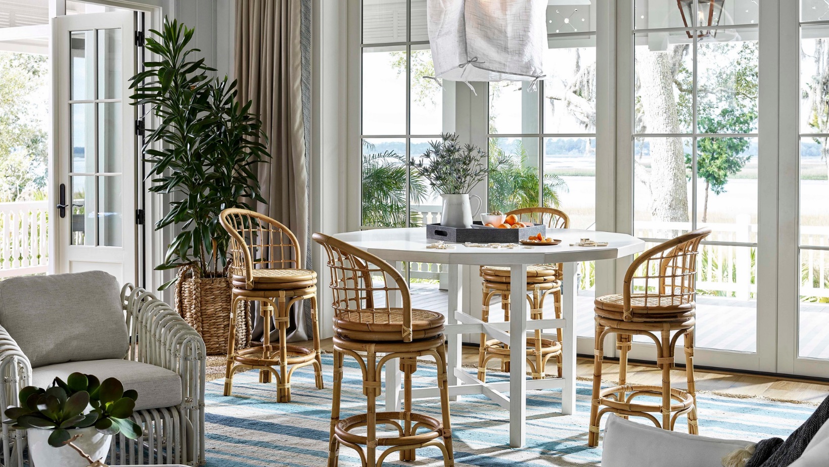 Coastal dining room with floor-to-ceiling glass, rattan seating and a water view, indoor-outdoor design by Landry Designs