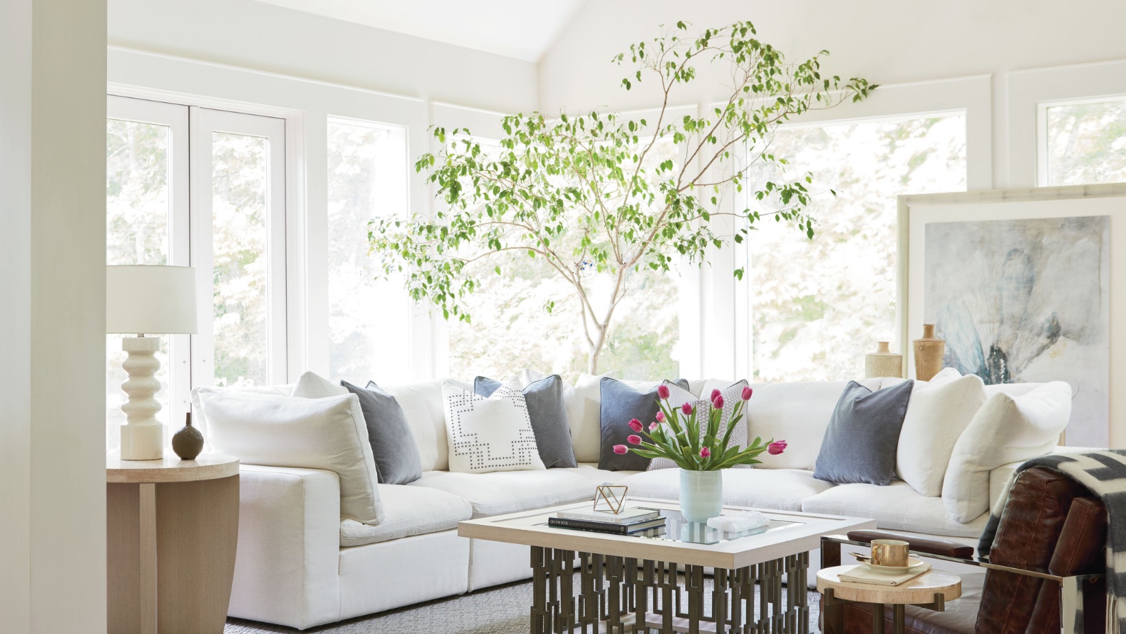 Bright living room with a large indoor tree, white sectional and garden views, biophilic interior design by Landry Designs
